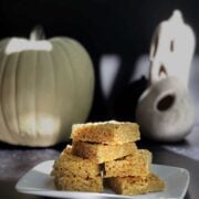 Pumpkin rice krispie treats stacked on a white plate with ghosts in the background.