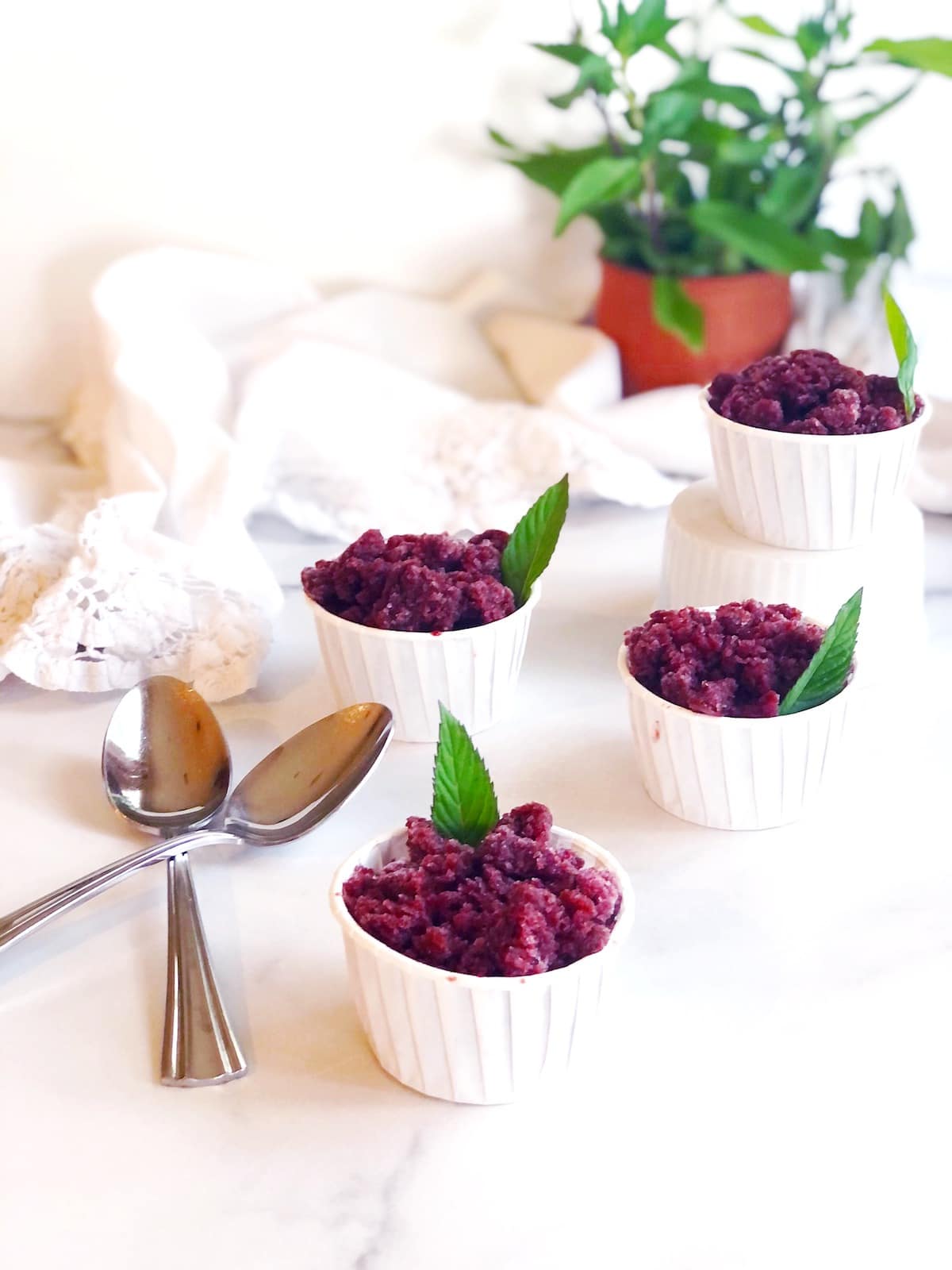 Four small bowls of cherry granita on a marble table.