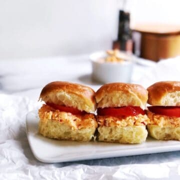 Pimento cheese sandwiches on a white plate with tomatoes.