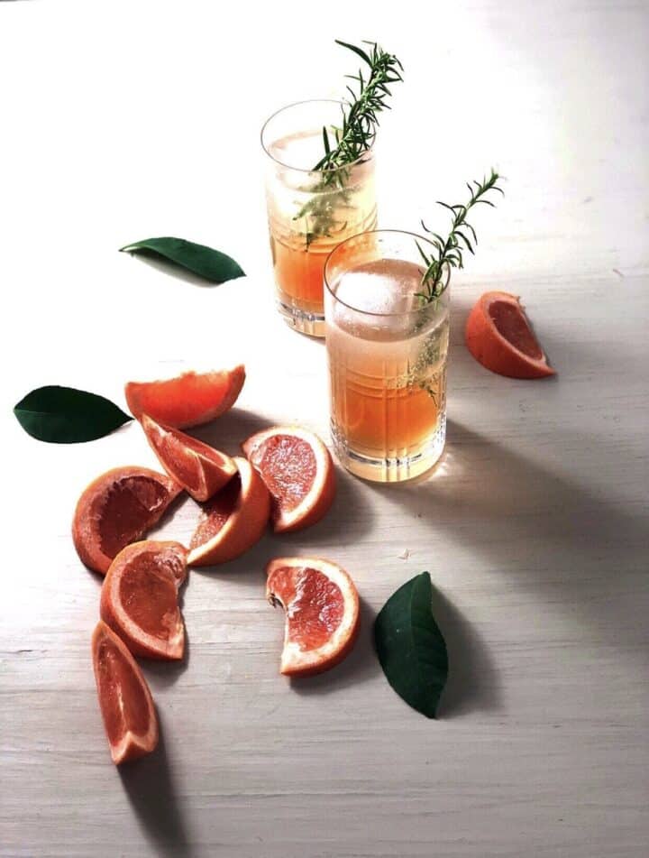 Two glasses of gin and tonic with grapefruit on a white board with multiple grapefruit wedges next to it.