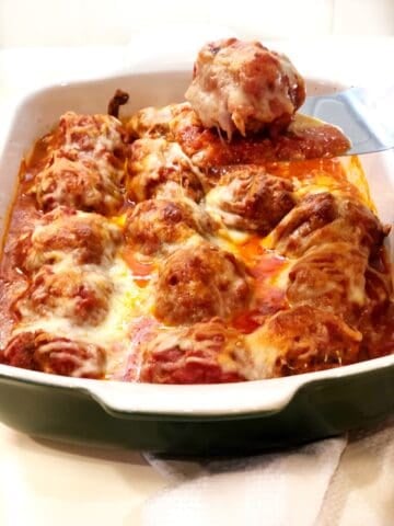 Baked meatball Parmesan with a spatula scooping out the meatballs.